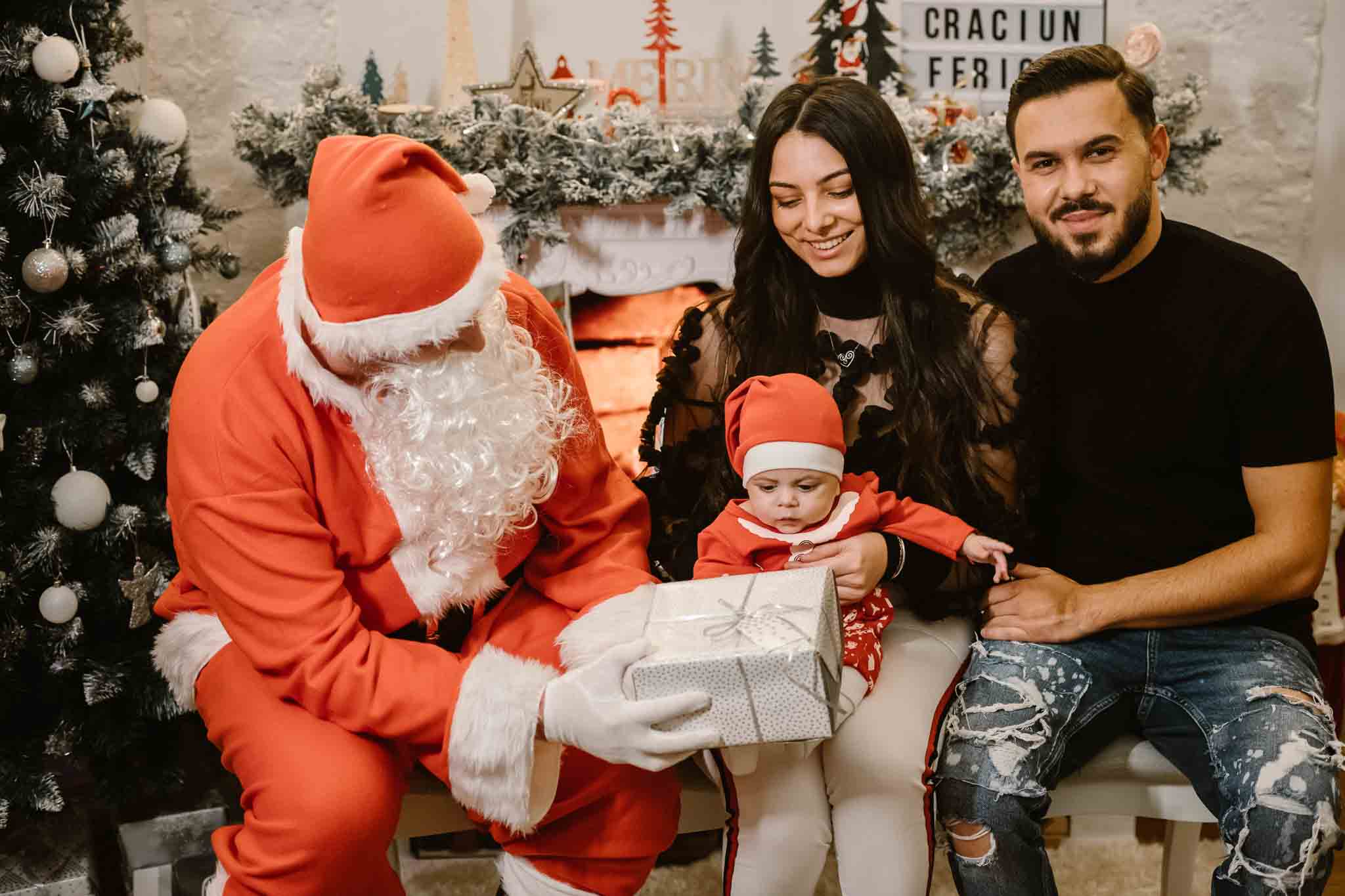 Fetiță îmbrățișându-și frățiorul mai mic, așezați pe perne pufoase în decor de Crăciun