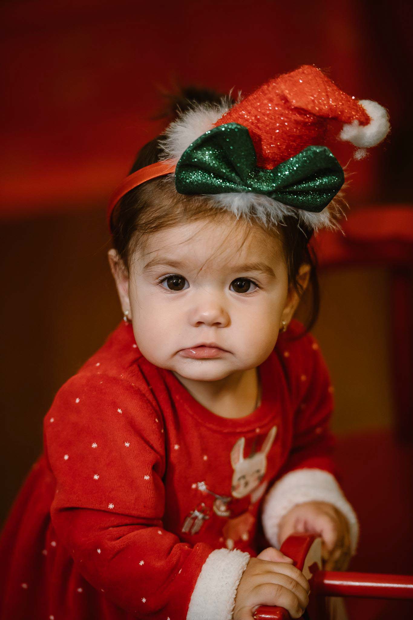 Portret de Crăciun cu fetiță mică, în rochie roșie și bentiță cu pălărie festivă verde-roșu