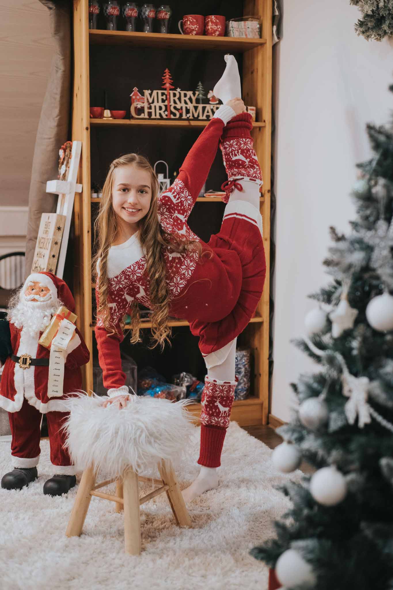 Portret de Crăciun cu adolescentă în salopetă roșie, executând o poziție de gimnastică lângă brad